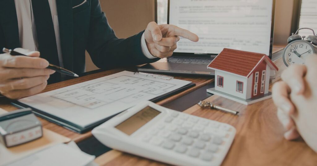 Asesor explicando documentos de compraventa de vivienda a un cliente con calculadora y papeles sobre la mesa