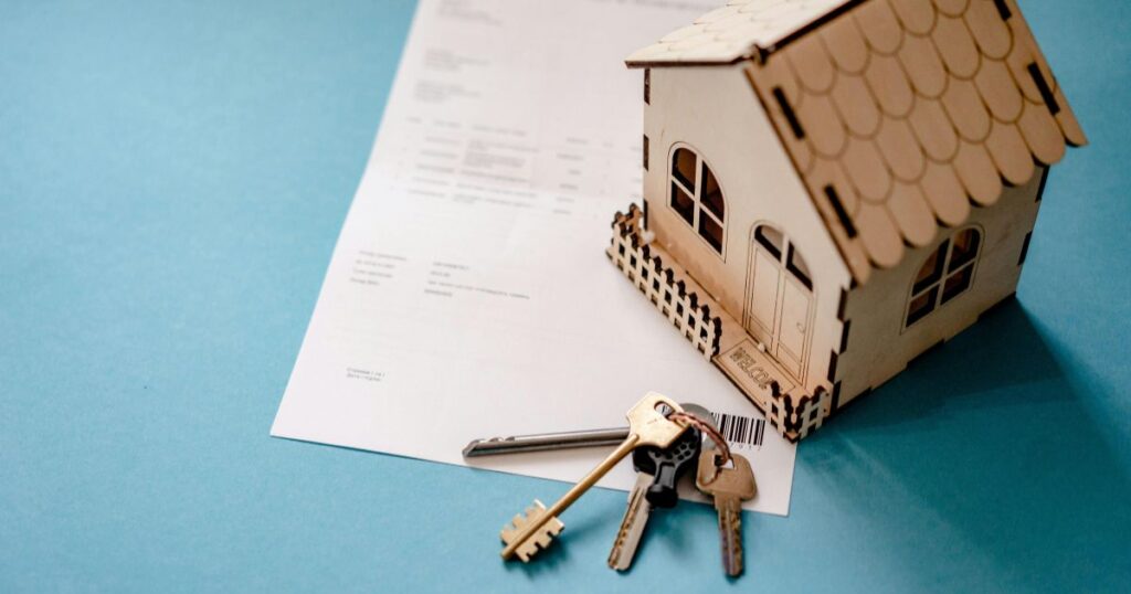 Llaves y contrato de una vivienda junto a una maqueta de una casa, representando la venta de un piso con inquilino.